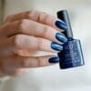 hand met donkerblauw gelakte nagels met een flesje 'Peacock Plume' van Gelzz