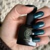 Hand met groen gelakte nagels wat een flesje Gelzz New glitter petrol vasthoud